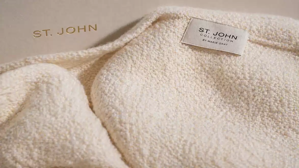 Close-up of a cream-colored St. John garment with label on a box background.
