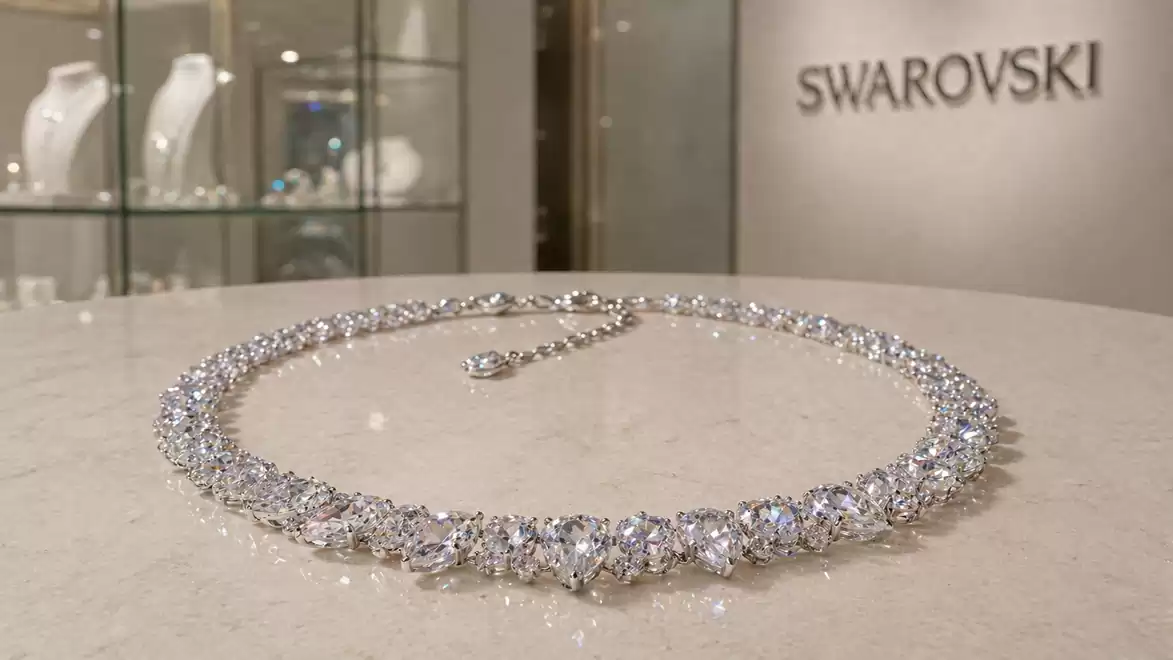 An elegant Swarovski diamond necklace on a table, with display cabinets of jewelry in the background.