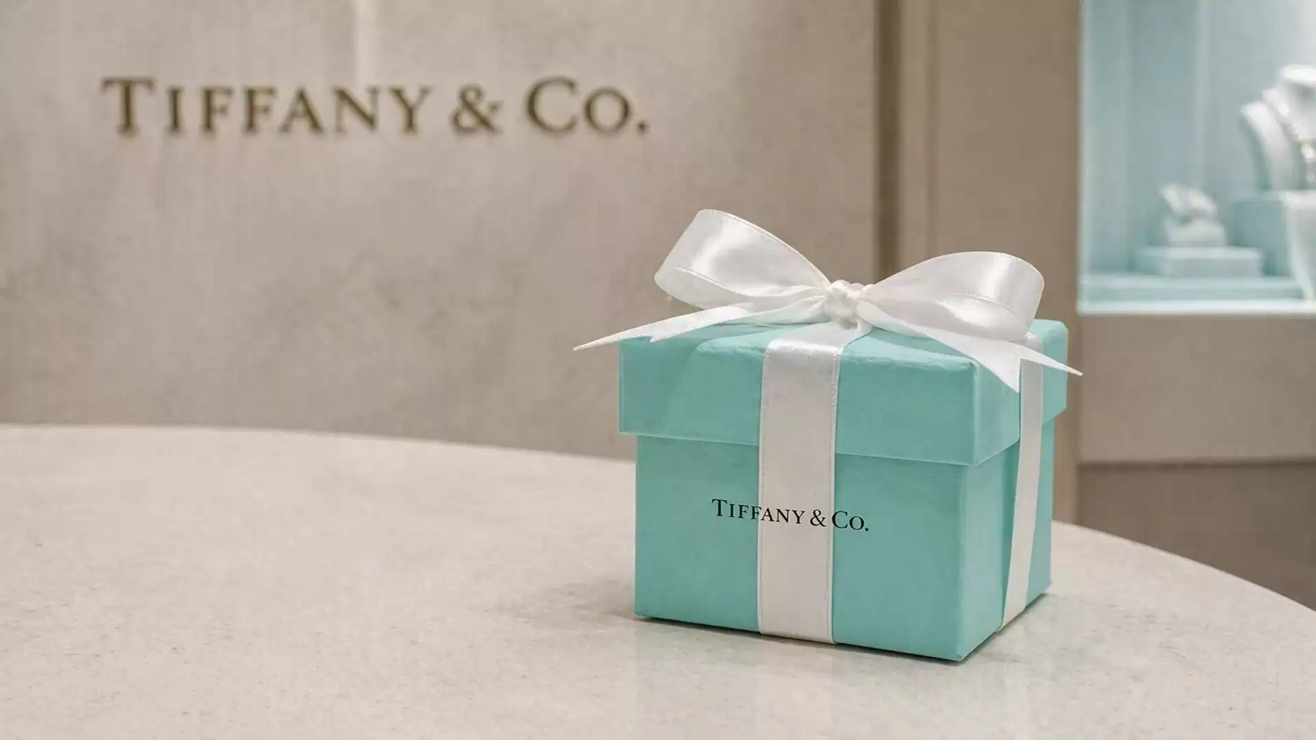 A Tiffany & Co. gift box with a white ribbon, on a table in a store.