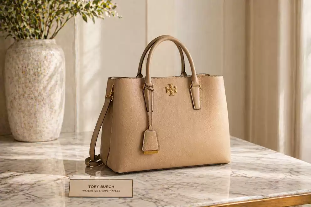 Elegant beige handbag on a marble table with green plant in the background.