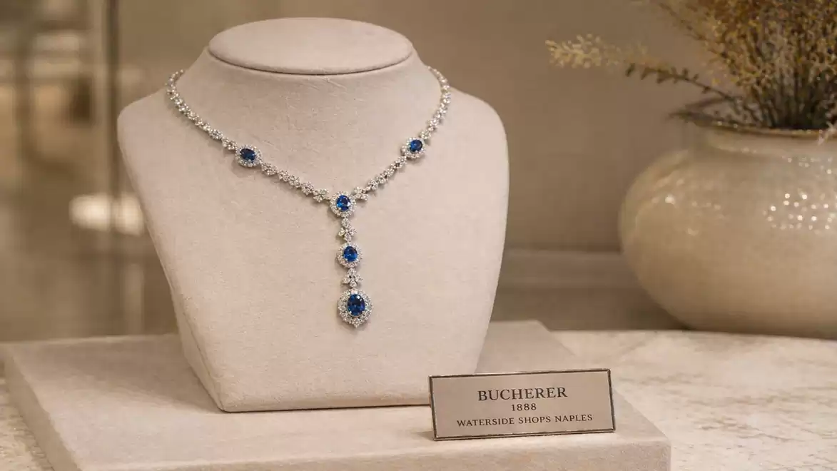 An elegant necklace with blue gemstones and diamonds, displayed on a white jewelry stand, accompanied by a plaque reading 'Bucherer 1888'.