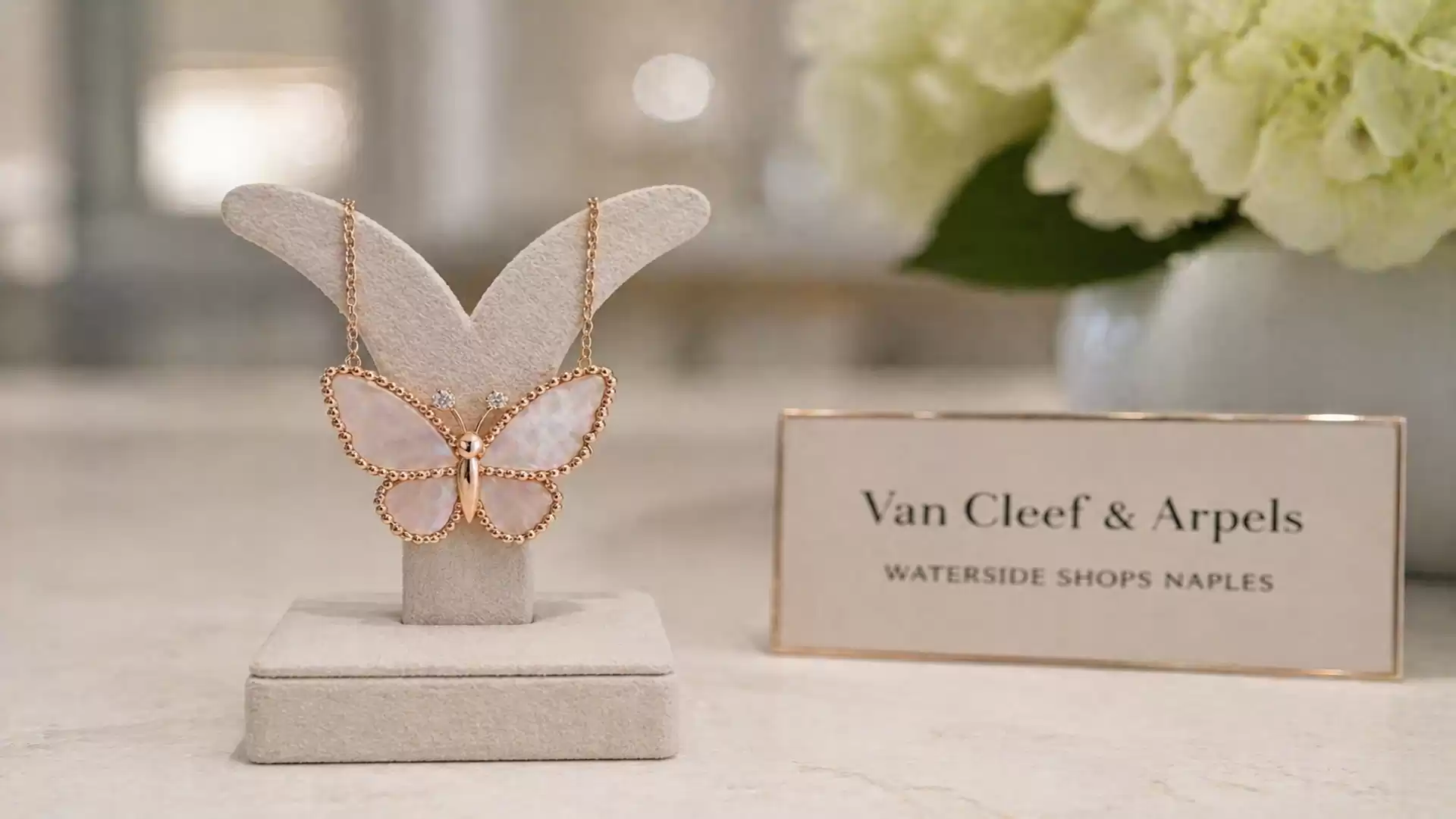 An elegant butterfly jewelry piece displayed at a Van Cleef & Arpels exhibition, presented on a white stand with a sign in the background.
