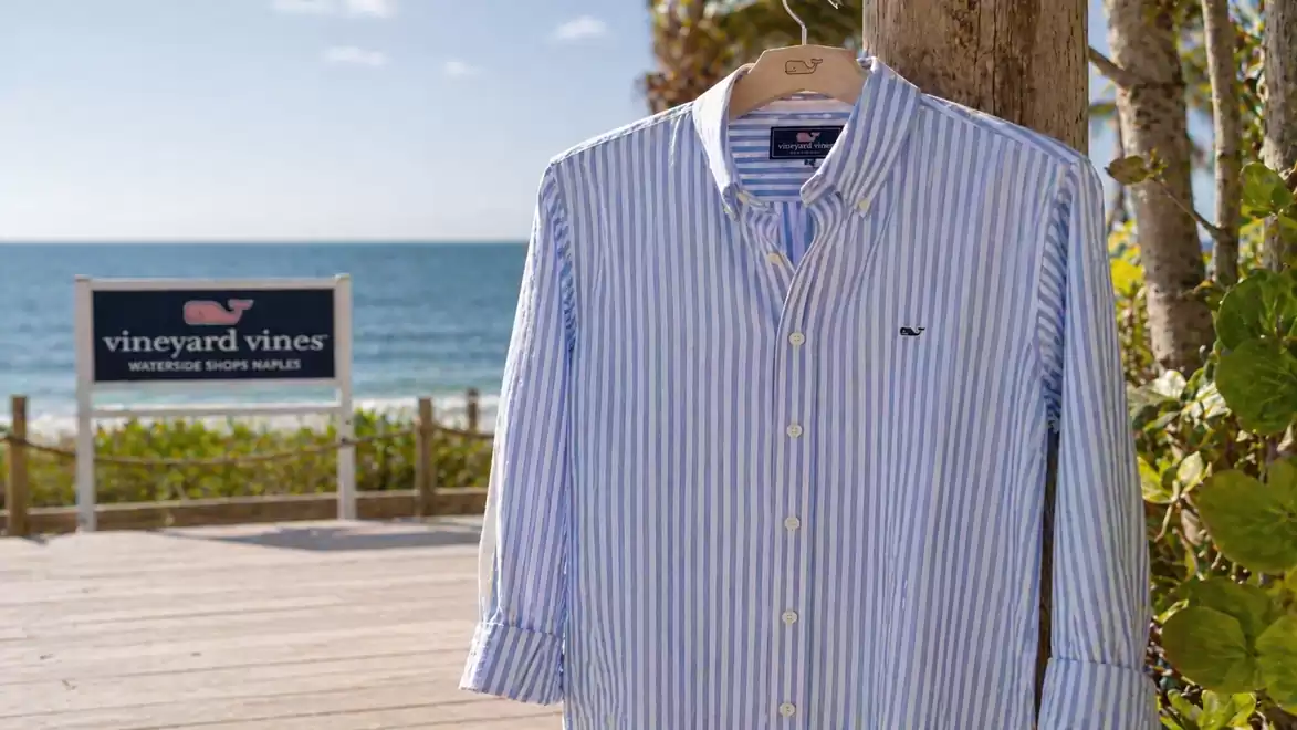 A striped shirt hangs on a tree overlooking the sea with a sign that says 'vineyard vines'.