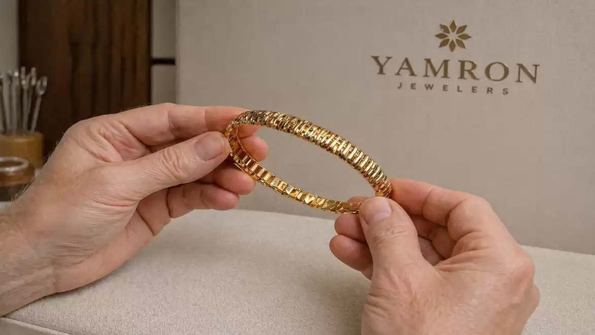 Close-up of two hands holding an elegant gold bracelet in front of a background with the inscription 'Yamron Jewelers'.