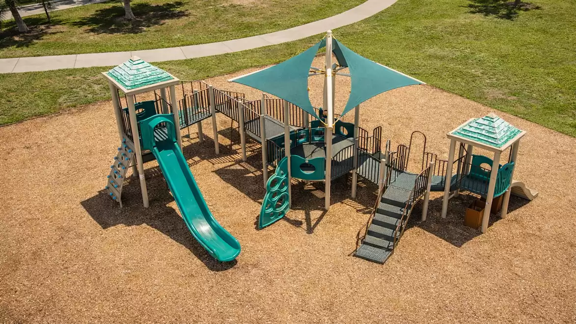 Aerial view of a playground with slides, climbing structures, and shade canopies, surrounded by grass.
