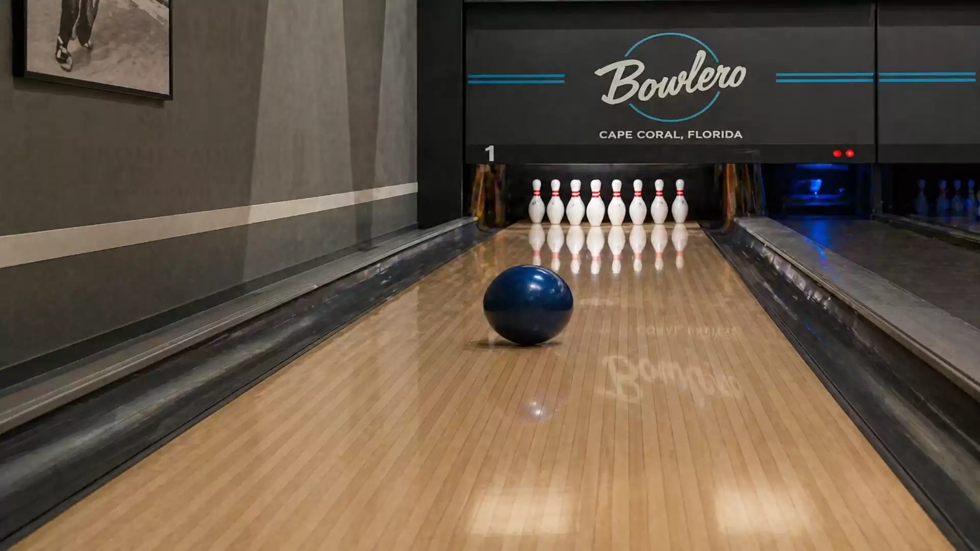 A bowling lane at Bowlero in Cape Coral, Florida, with a blue bowling ball rolling towards the pins.