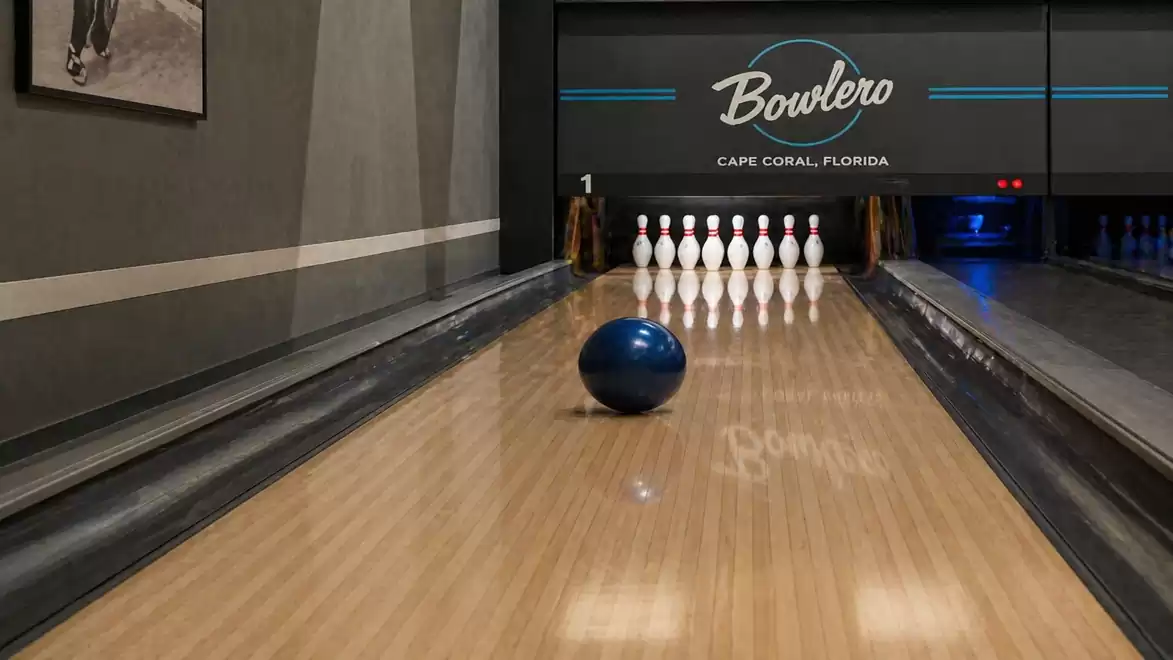 A bowling lane at Bowlero in Cape Coral, Florida, with a blue bowling ball rolling towards the pins.