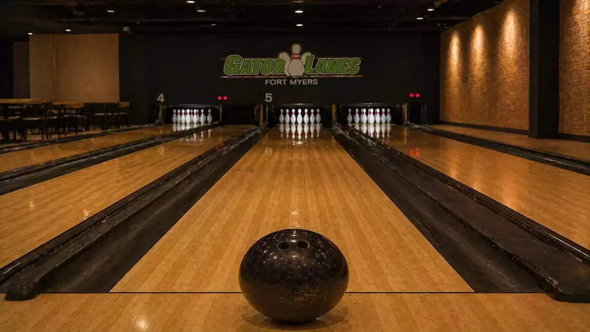 Interior view of a modern bowling alley with several lanes and a dark bowling ball in the foreground.