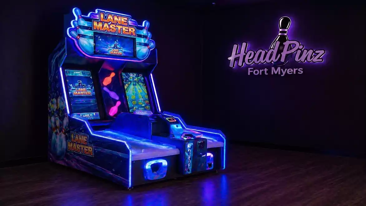 An illuminated arcade machine labeled 'Lane Master' in a gaming hall with a dark background and the 'HeadPinz Fort Myers' logo on the wall.