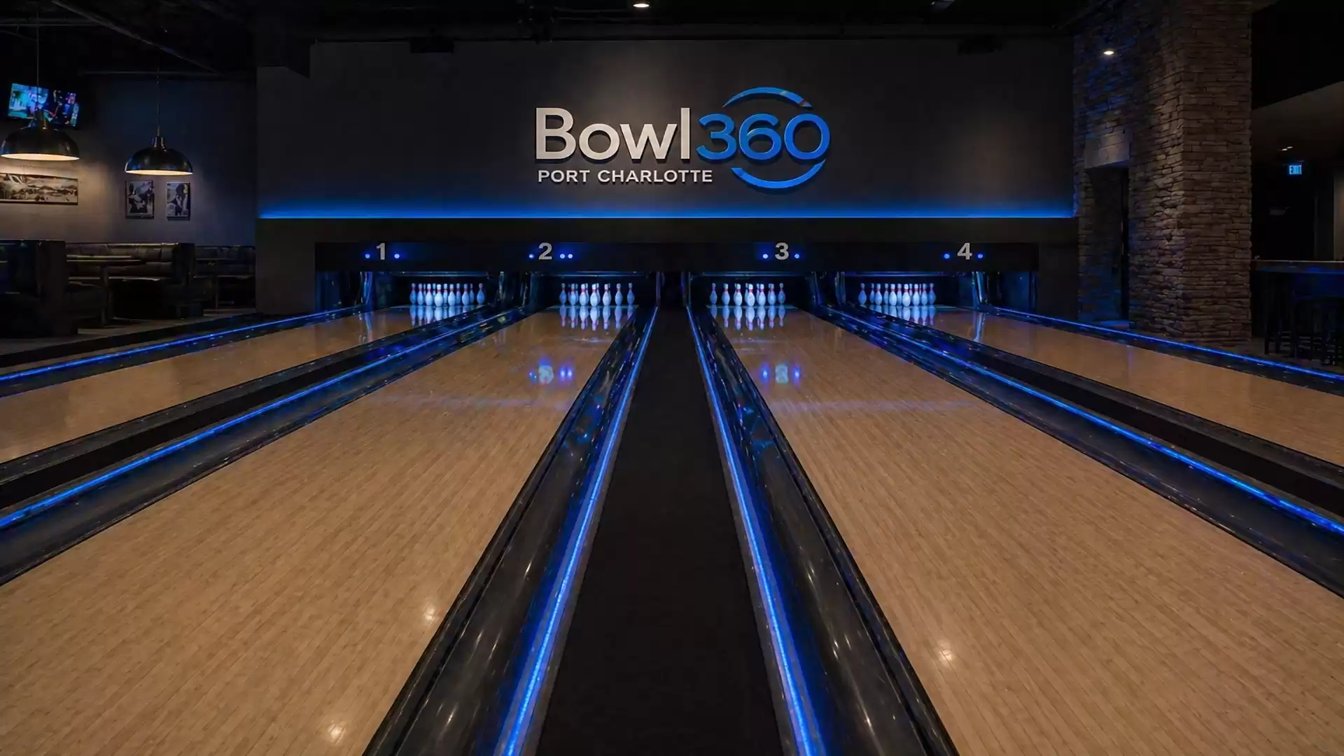 Interior view of a modern bowling alley, illuminated with blue lights. The sign 'Bowl 360 Port Charlotte' is visible in the background, surrounded by multiple lanes.