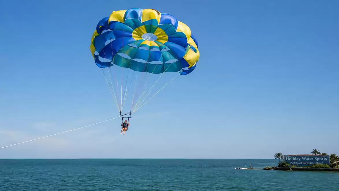 People parasailing over the sea with a colorful parachute under a clear blue sky.