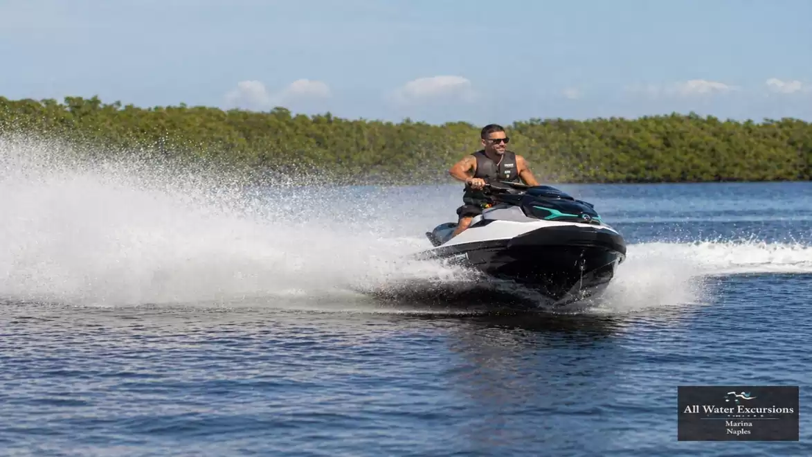 Person riding a jet ski on the water under sunny skies, leaving a trail of spray behind.