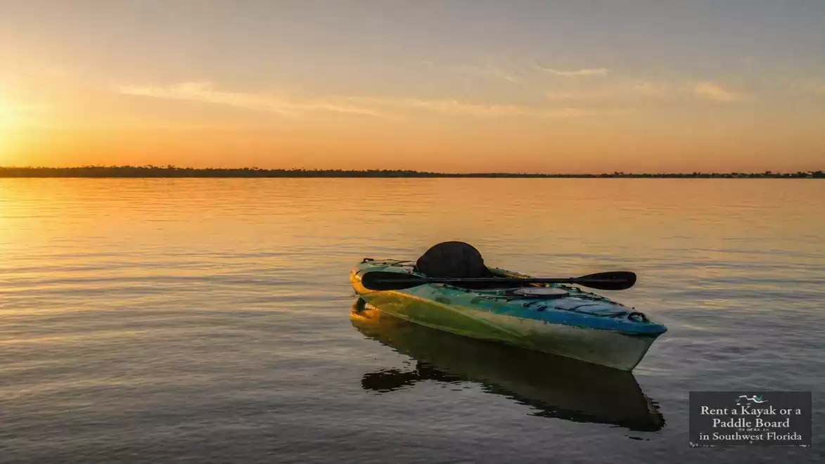 A single kayak floats on a calm lake at sunset.