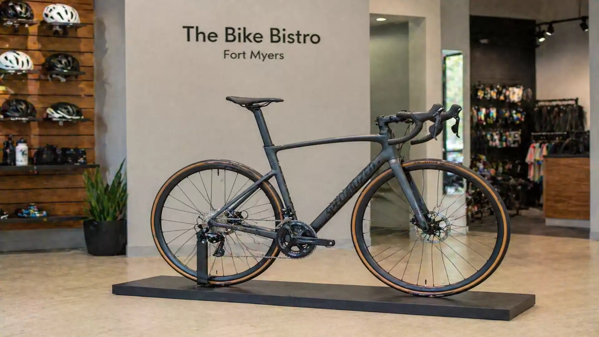 A modern road bike is displayed in a stylish bike shop called 'The Bike Bistro' in Fort Myers, surrounded by accessories and bicycle helmets on the wall.