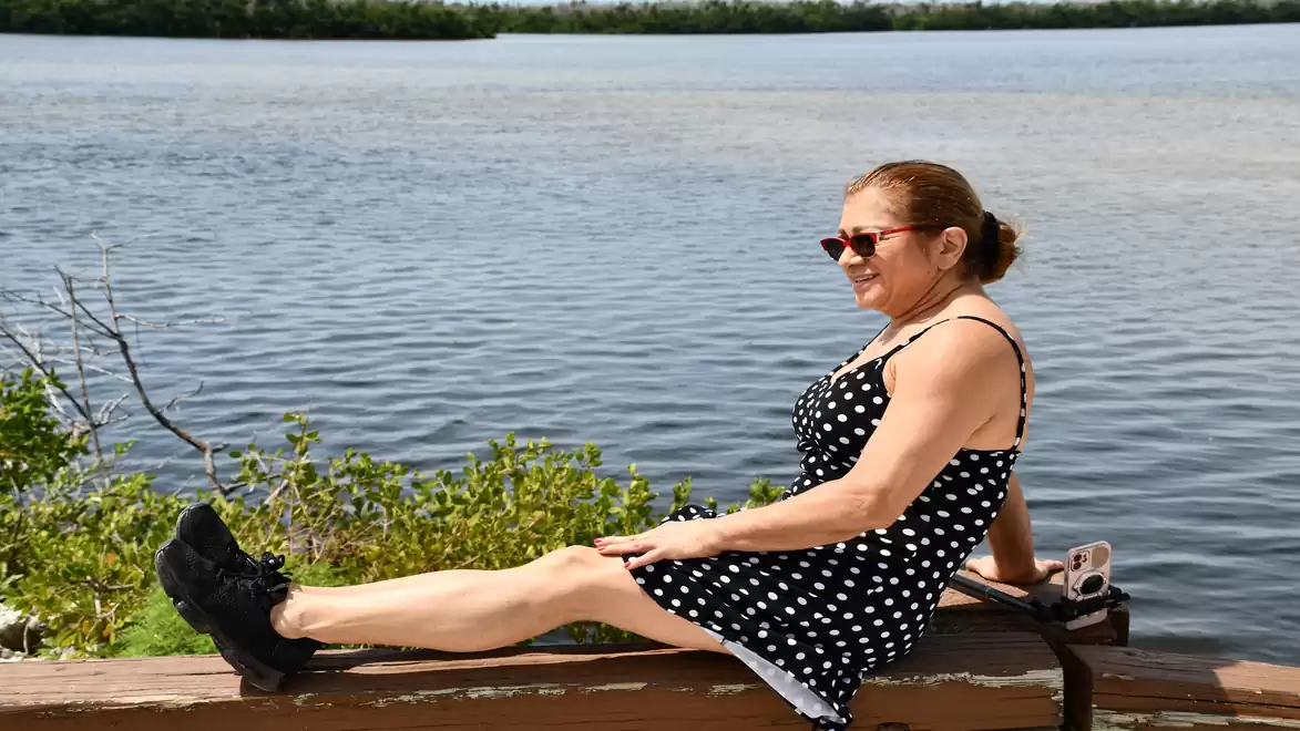 Woman in a polka dot dress sitting by a riverside, looking at the water and enjoying the sun.