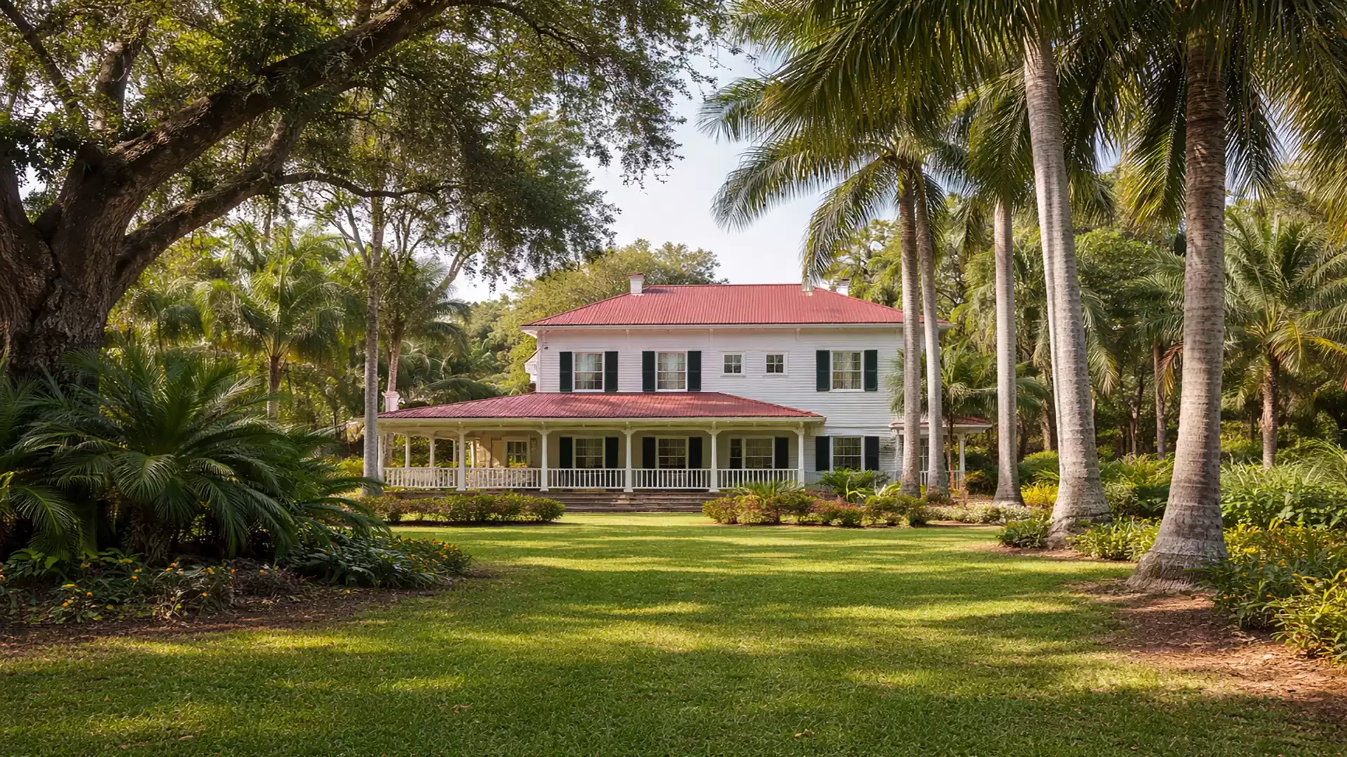 Large white house with a red roof, surrounded by palm trees and a manicured lawn.