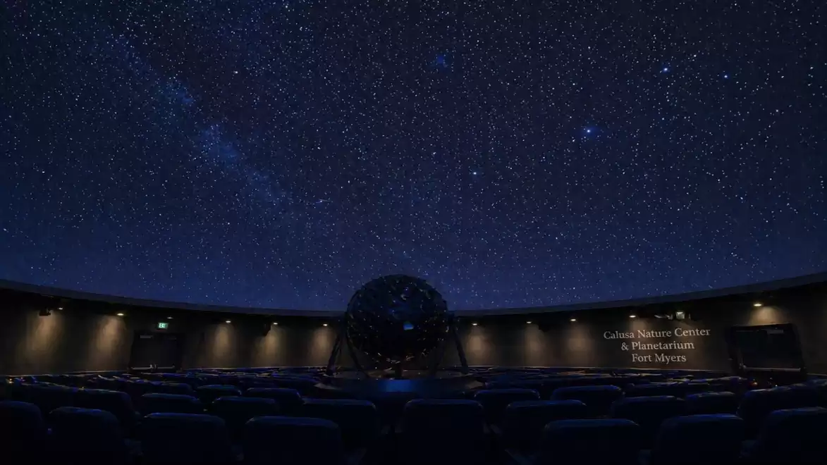 Interior view of a planetarium with a projector dome under a glowing starry sky.