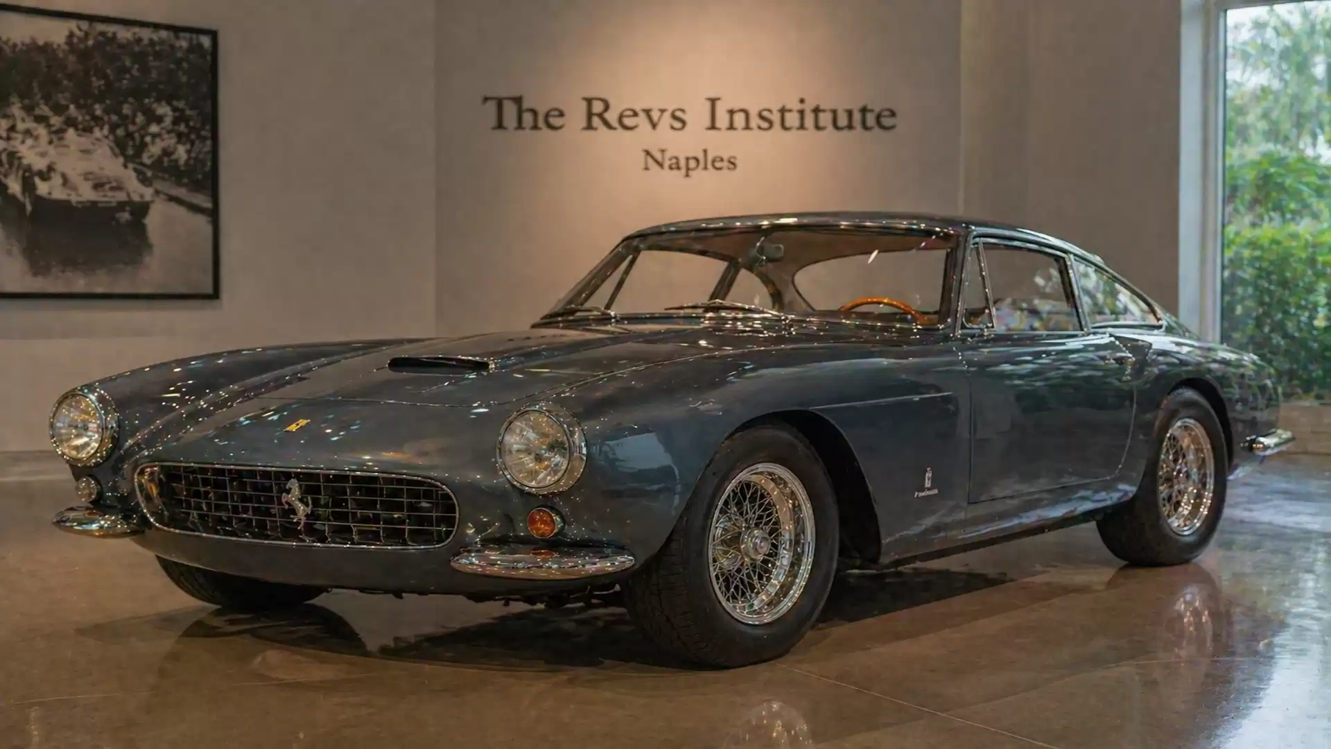 A classic blue sports car displayed at the Revs Institute in Naples, showcased on a shiny floor.