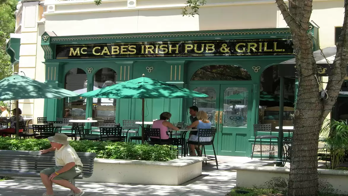 Exterior view of a traditional Irish Pub and Grill with green doors and umbrellas, people sitting outside.