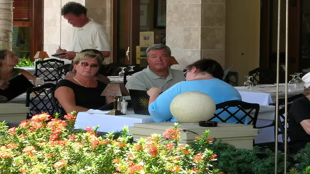 People sitting outdoors at a restaurant enjoying a meal with flowers in the foreground.
