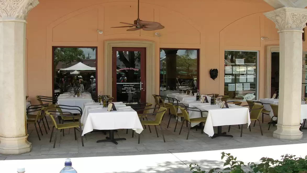 Outdoor area of a restaurant with set tables and chairs under a covered area with columns.