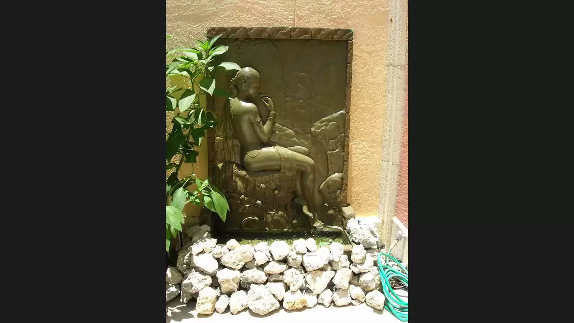 A wall relief with a seated figure and a plant in the garden, surrounded by stones.
