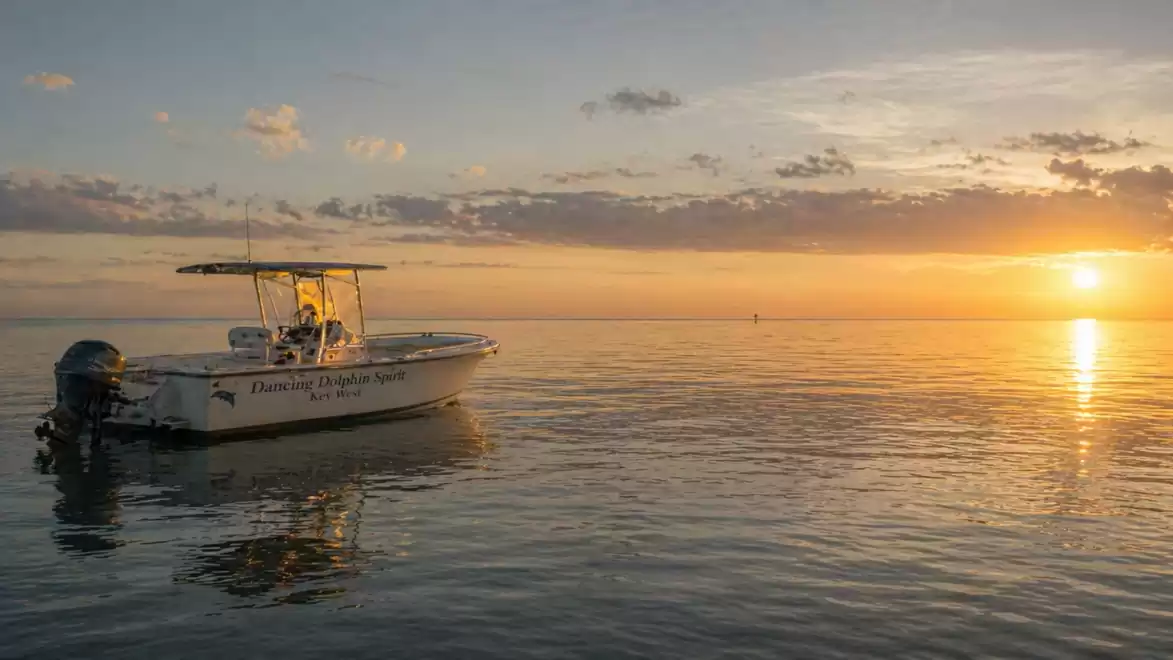 A small motorboat on a calm sea at sunset with an orange sky and reflection on the water.