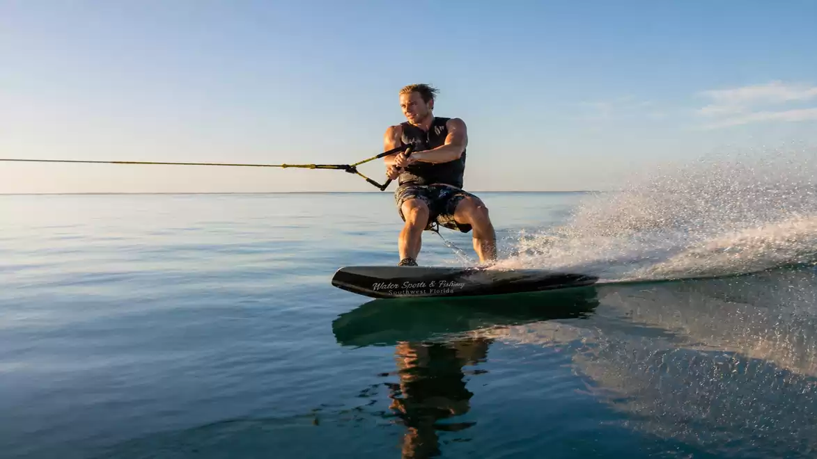 A man wakeboarding on calm water under a blue sky.