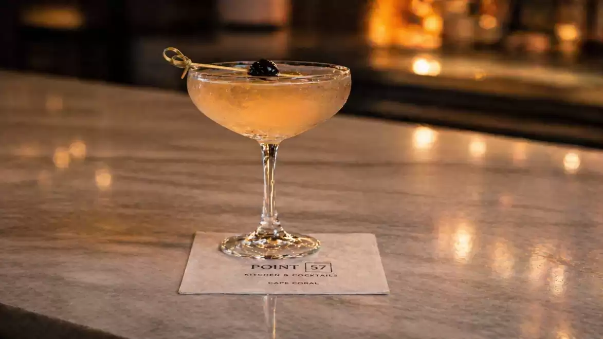 An elegant cocktail with a black cherry, served in a coupe glass on a marble bar surface.