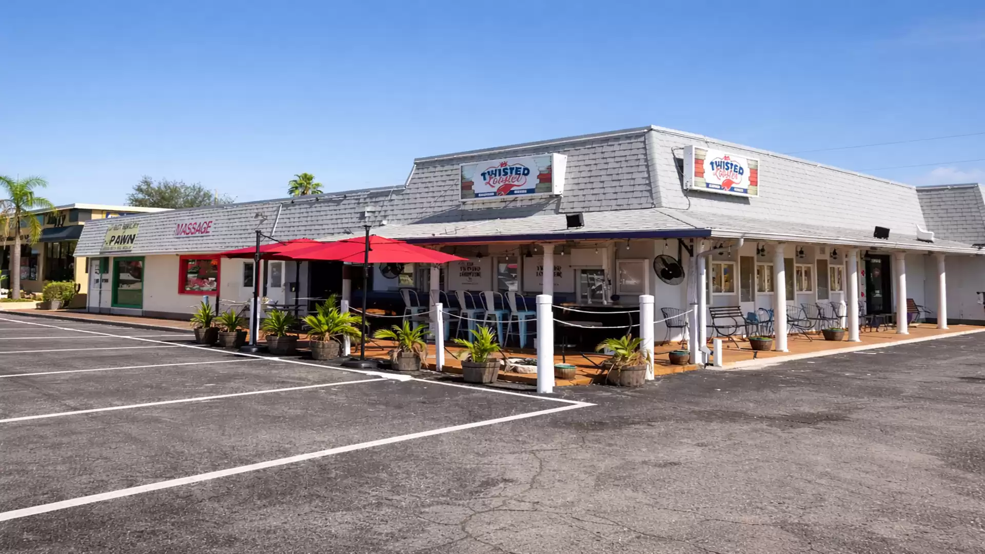 A small retro-style restaurant with outdoor seating and red umbrellas on an empty parking lot under a clear sky.
