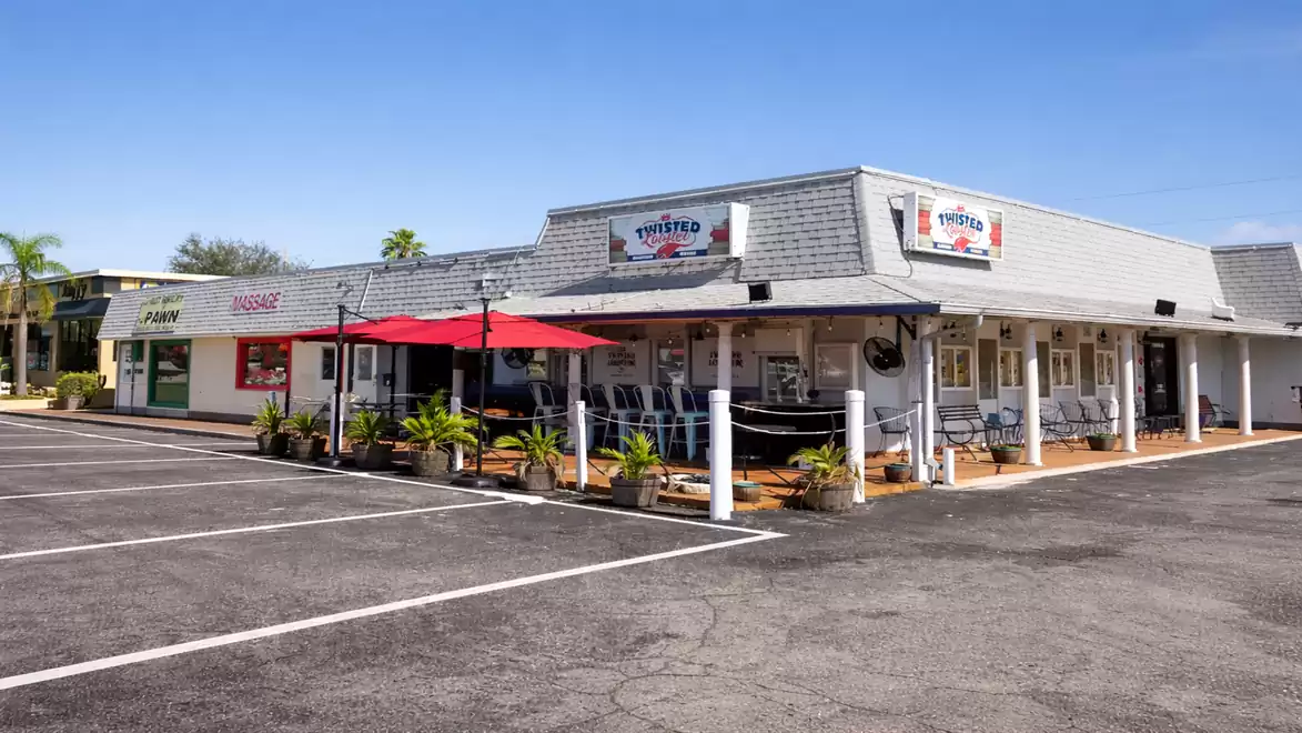 A small retro-style restaurant with outdoor seating and red umbrellas on an empty parking lot under a clear sky.