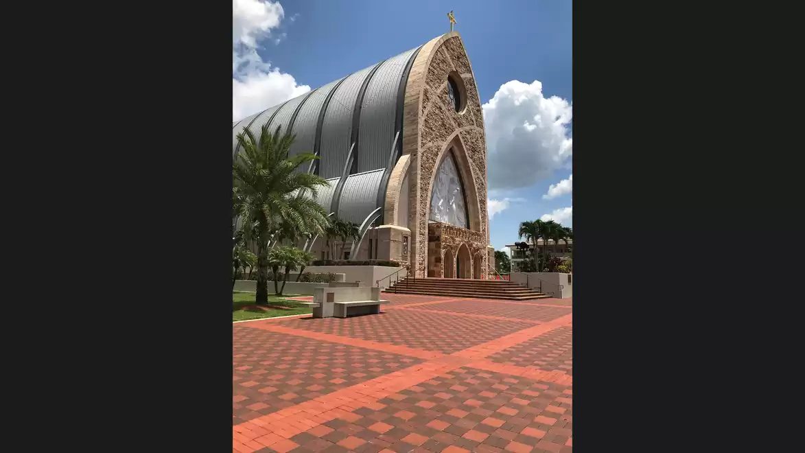 A modern church with an arched roof and glass windows under a blue sky with clouds.