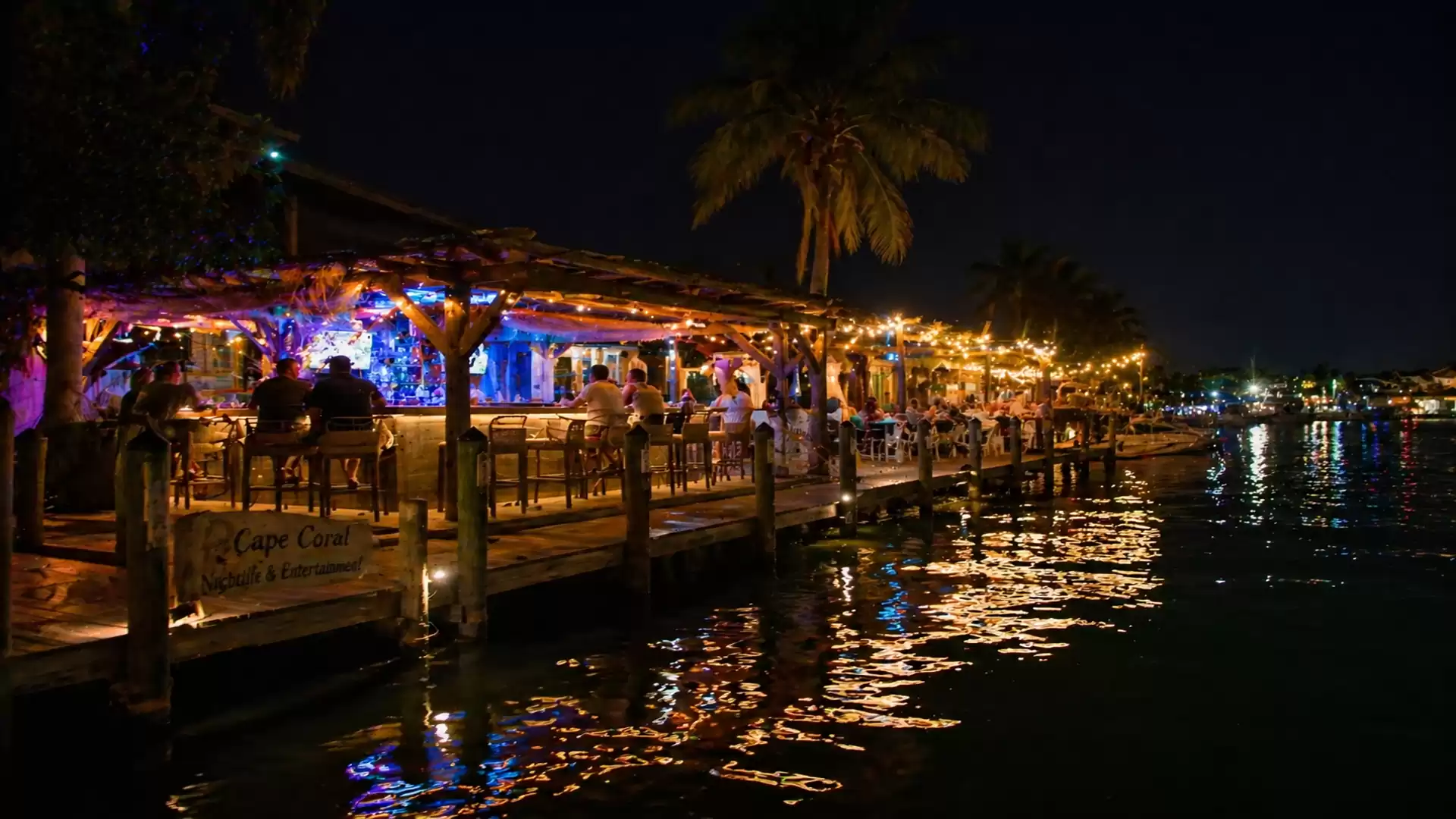 A mood-lit restaurant on a pier by the water in a tropical setting at night.