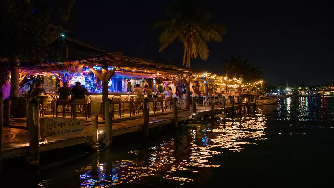 A mood-lit restaurant on a pier by the water in a tropical setting at night.