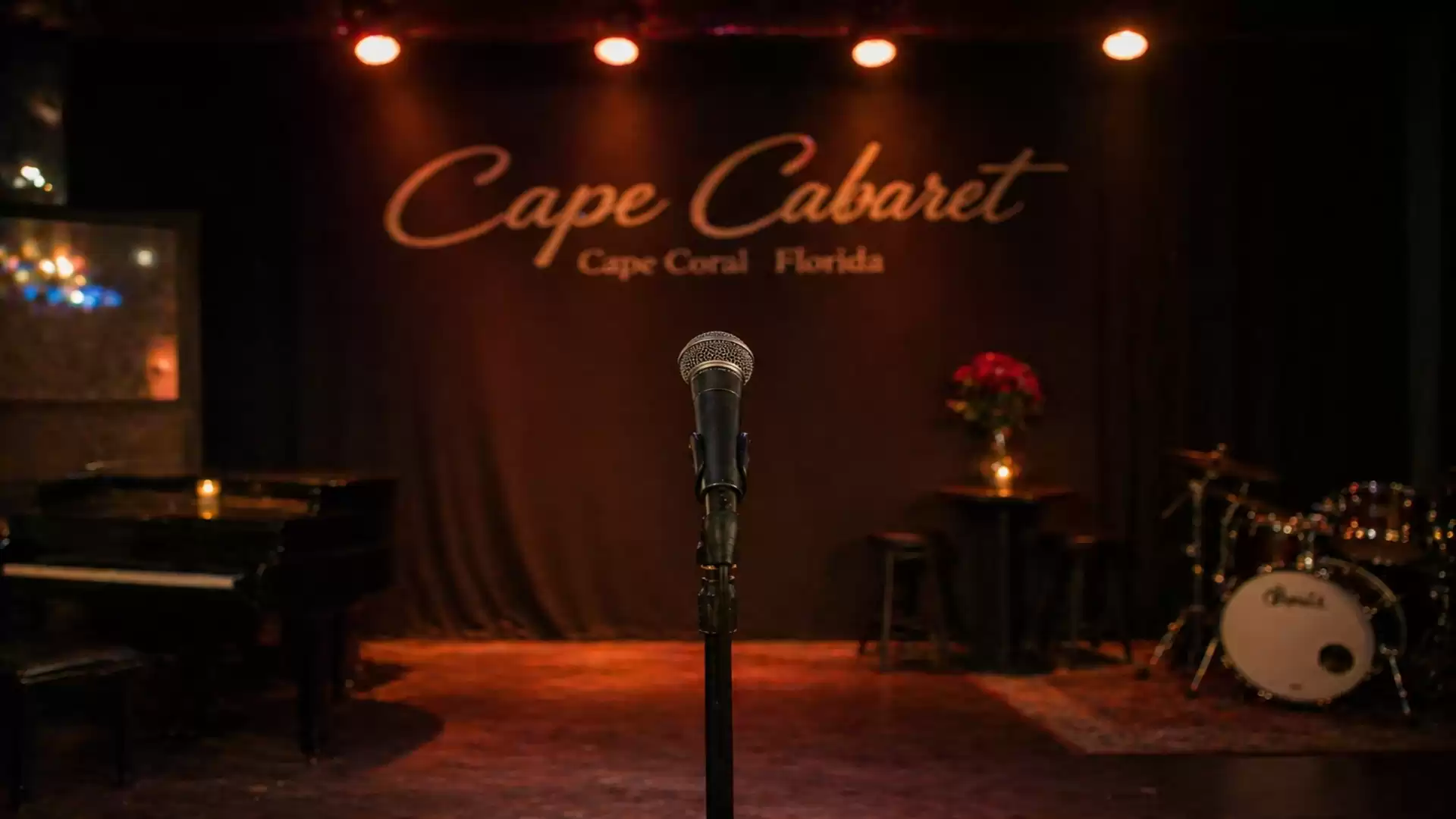 Stage with microphone at Cape Cabaret, Cape Coral, Florida. A grand piano, flowers on a table, and a drum set in the background.