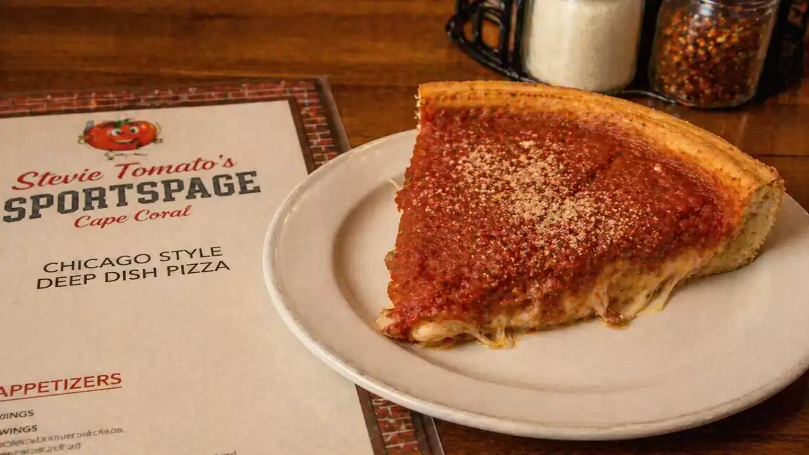 A slice of Chicago Style Deep Dish Pizza on a plate next to a restaurant menu.