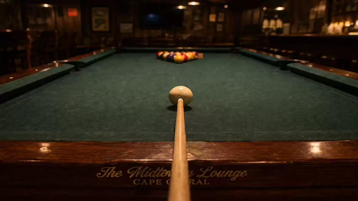 A billiard table in a dimly lit room with a cue aimed at the white ball.