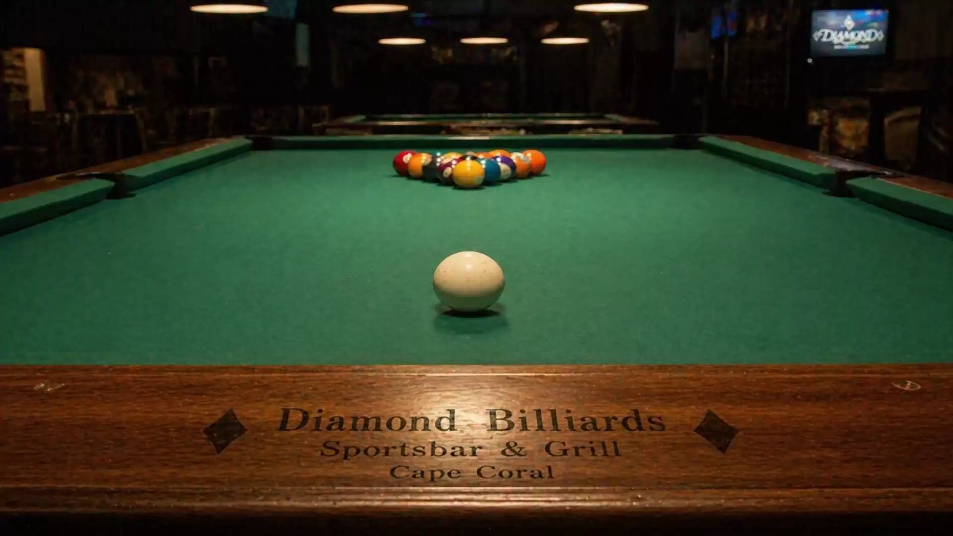 A billiard table in a sports bar with arranged billiard balls and a cue ball in the foreground.
