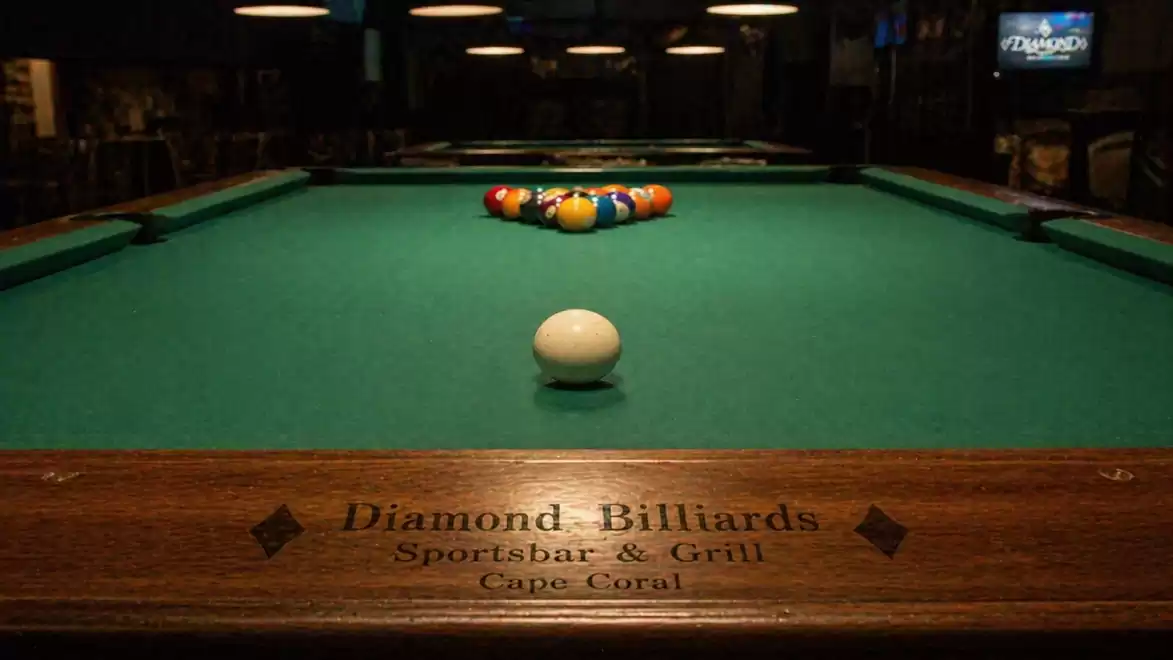 A billiard table in a sports bar with arranged billiard balls and a cue ball in the foreground.