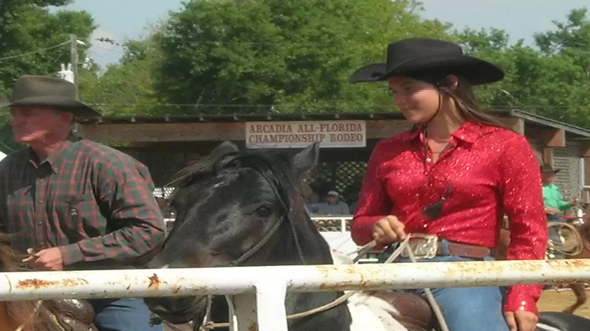 Two people in cowboy attire riding horses at a rodeo event.