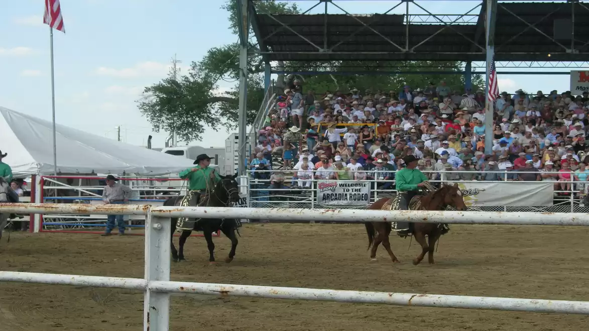 Rodeo riders in an arena with a crowd of spectators in the stands.