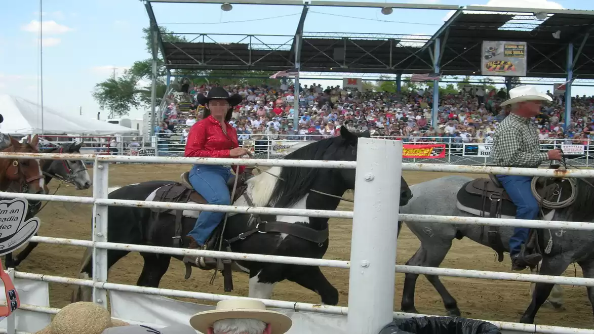 Rodeo with riders in traditional attire in front of a large audience under a covered stadium.