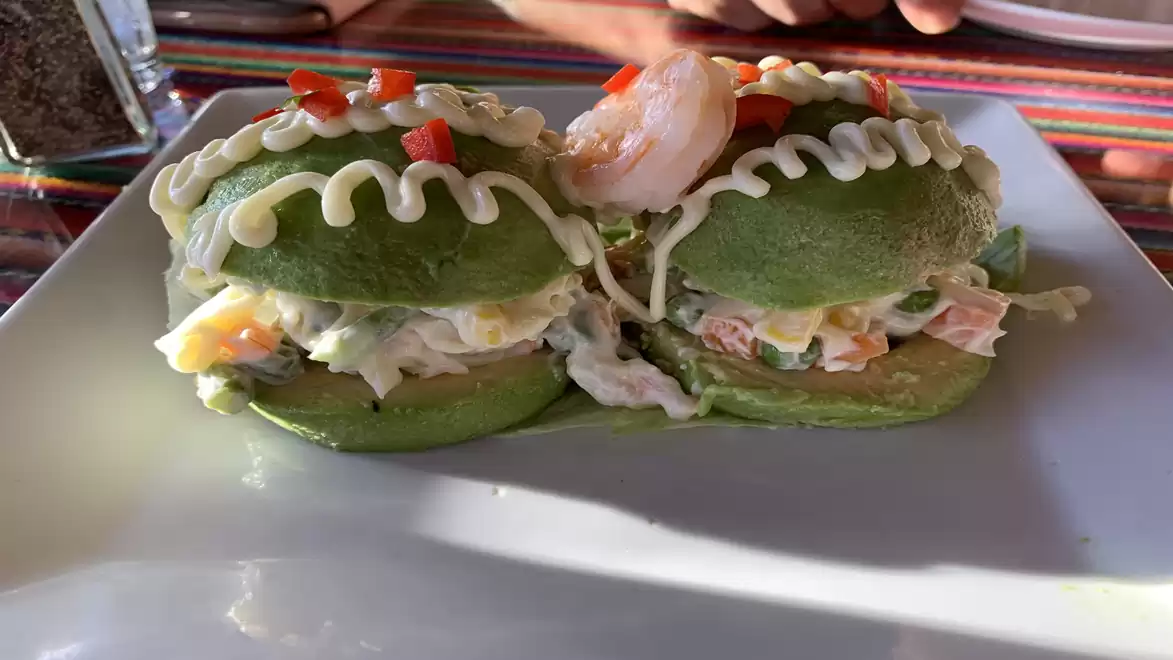 A plate featuring two halves of a savory avocado with shrimp filling, garnished with cream and bell peppers, on a white plate on a colorful striped tablecloth.
