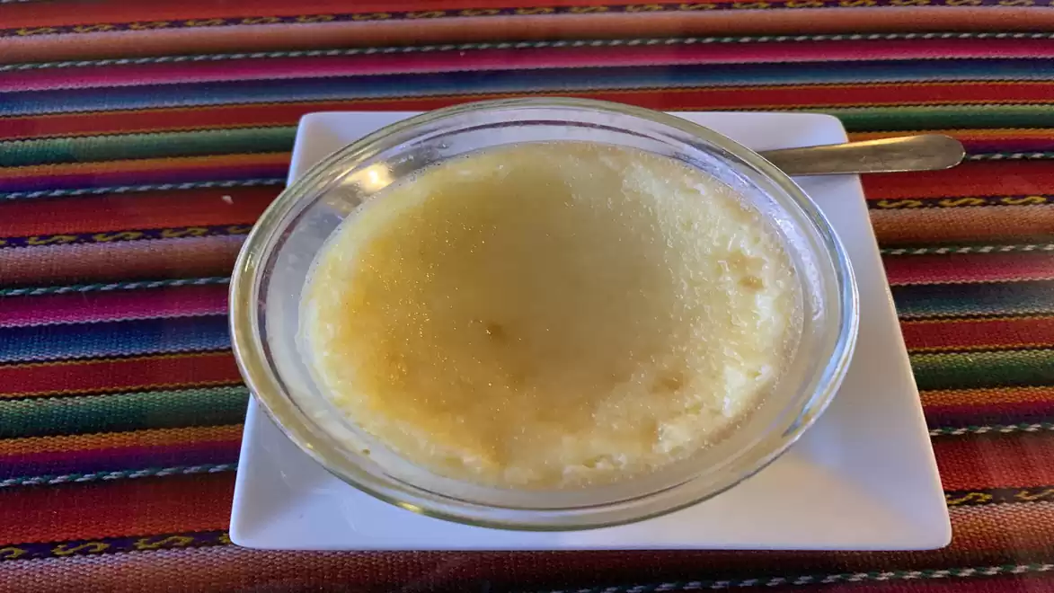 A bowl of vanilla pudding on a flat white plate, placed on a colorfully striped table.