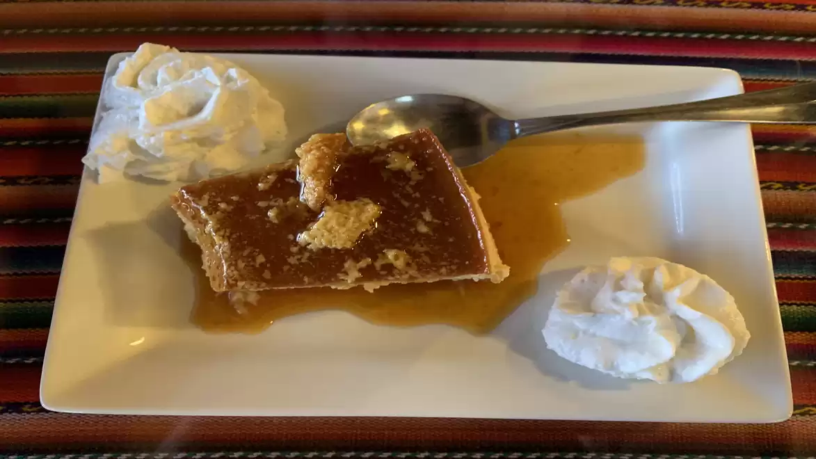 A rectangular cake on a white plate, garnished with whipped cream on two sides. A spoon is beside the cake, which is drizzled with syrup.