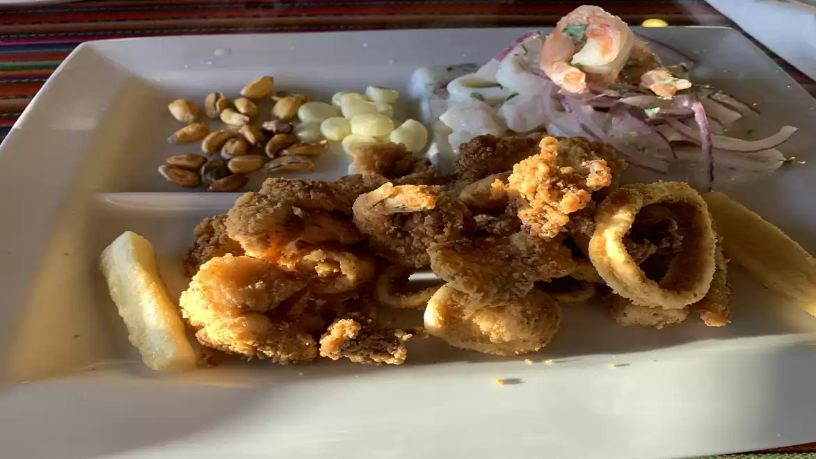 A delicious seafood platter featuring fried calamari, corn nuts, and fresh ceviche with lime, served on a rectangular white plate.