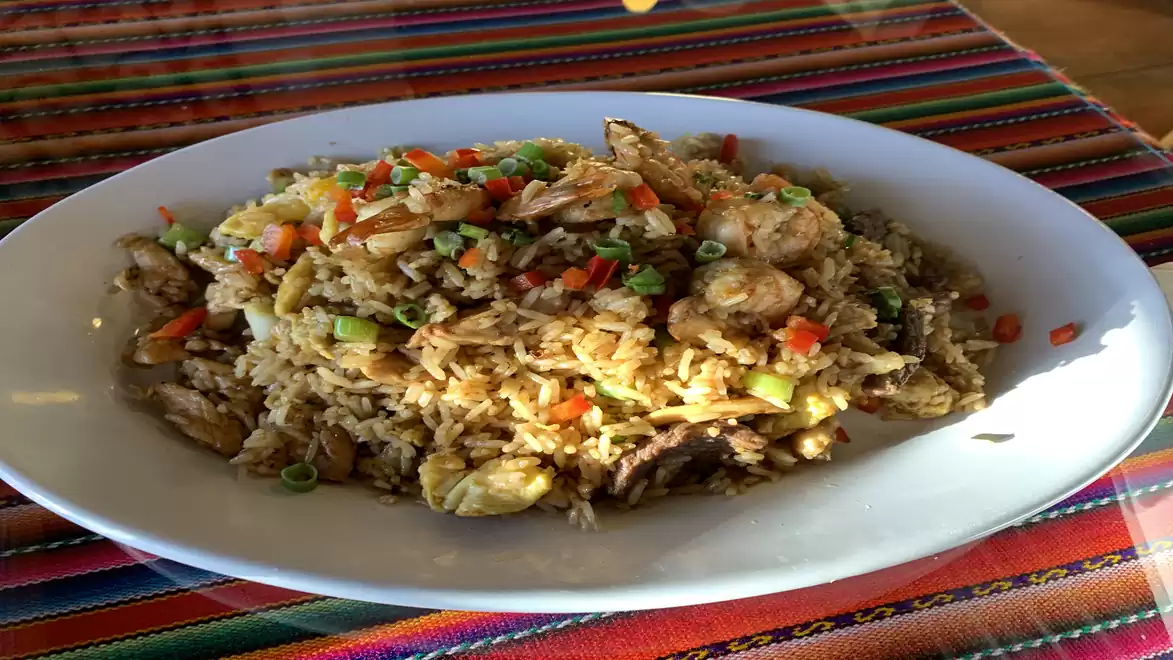 An oval plate with fried rice mixed with bell peppers, spring onions, and chicken pieces on a colorful table runner.