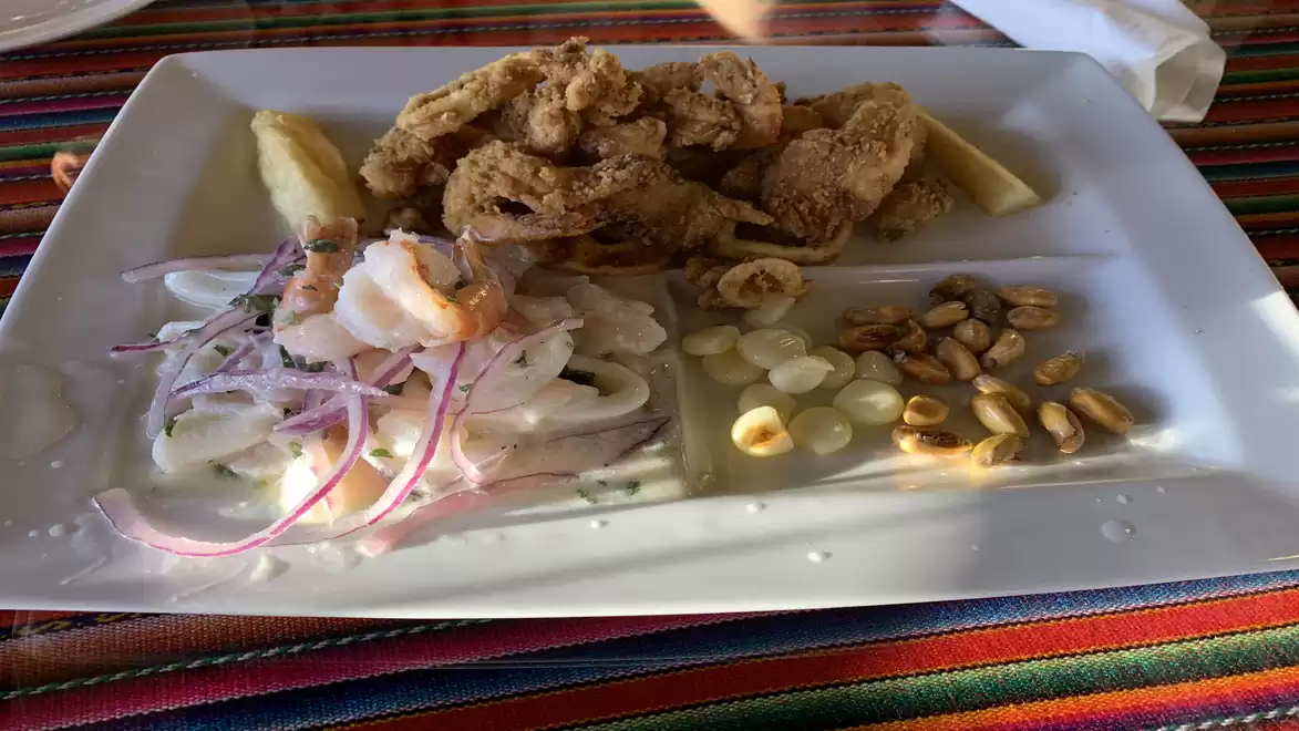 A plate with ceviche, onions, fried fish, and roasted corn on a colorful tablecloth.