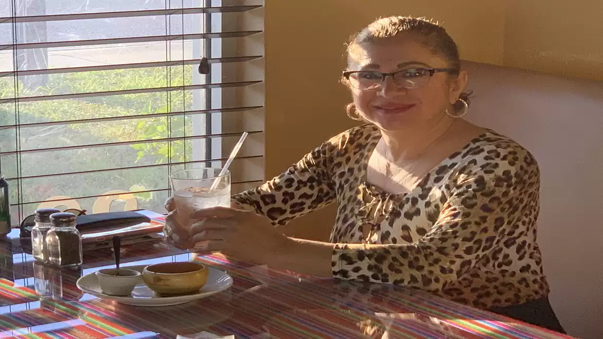 Woman in leopard print shirt enjoying a drink at a table in sunlight.