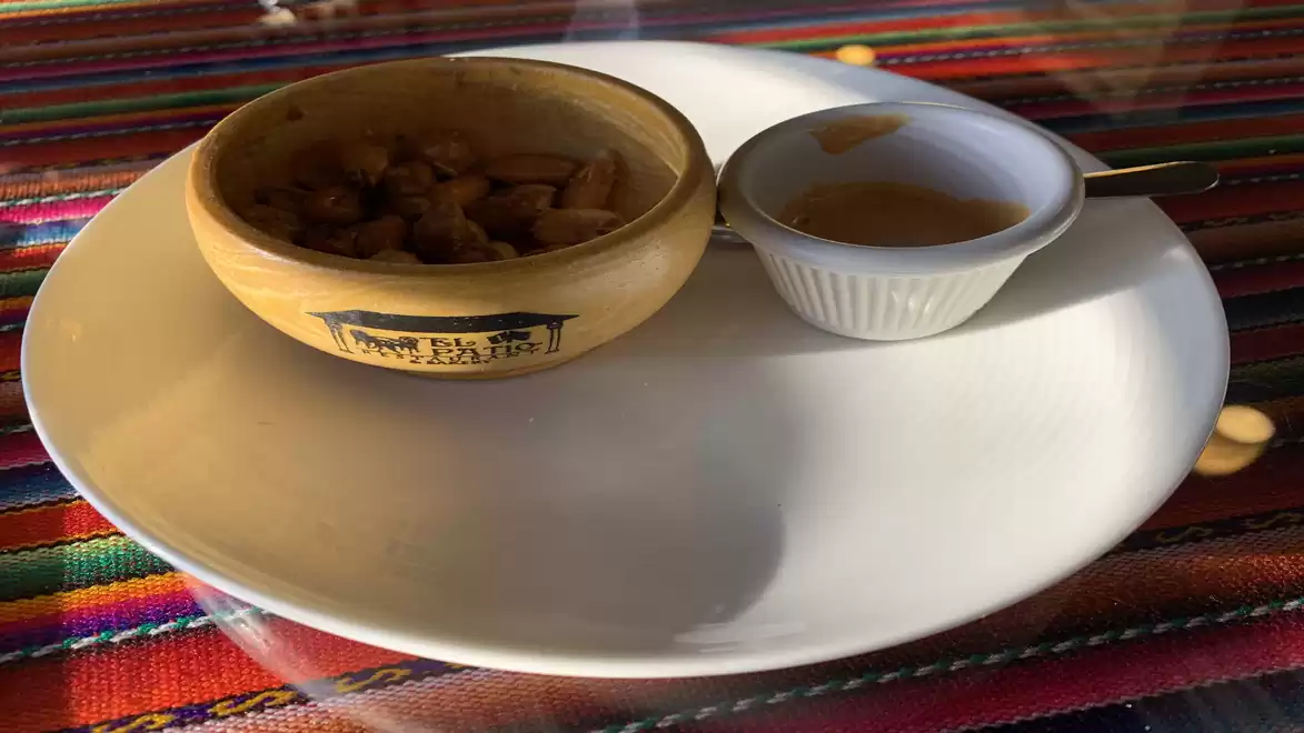 A wooden bowl with filling next to a small white bowl with sauce, placed on a white plate. The background is a colorful, striped table runner.